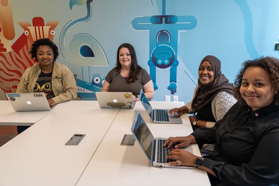 Four women sitting at laptops and smiling.