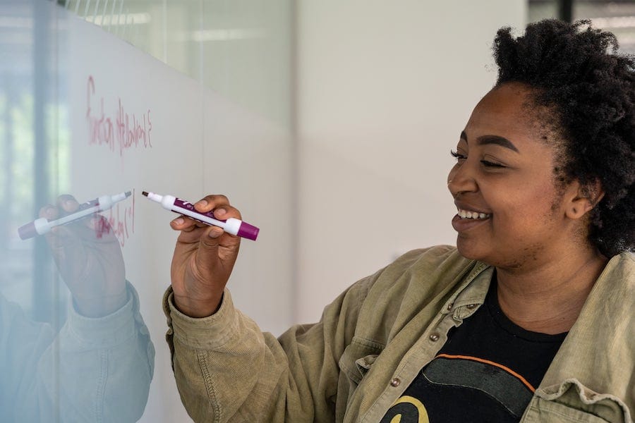 Black woman coding on a whiteboard.