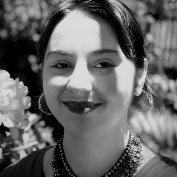 Margaret Fero, a white nonbinary person with their hair up, smiles at the camera in high-contrast lipstick